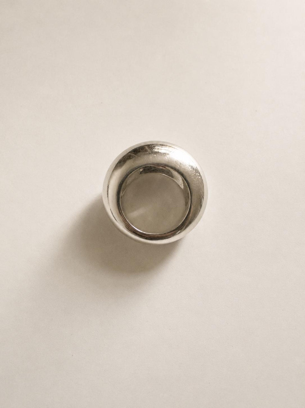 A polished silver ring with a wide, rounded band, photographed from directly above on a light beige background.